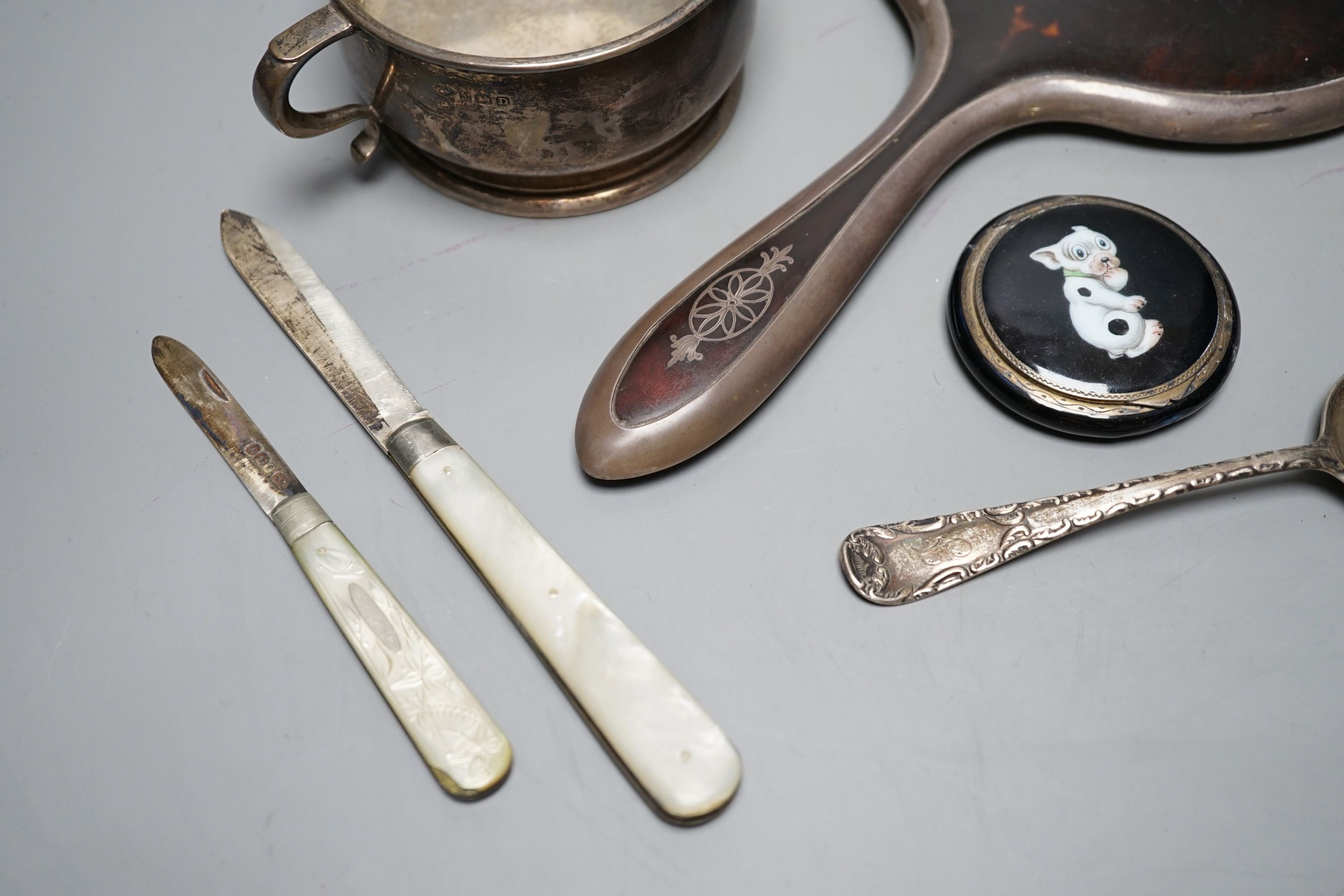 A silver two handled bowl, a silver mounted hand mirror, two silver and mother of pearl fruit knives, a silver preserve spoon and enamelled compact decorated with a dog.